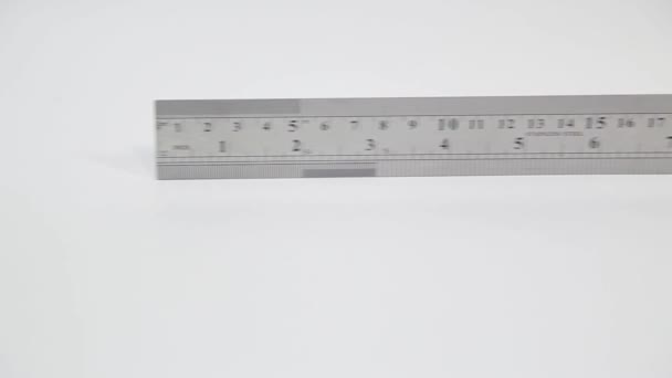 Panoramique lente de la règle en acier inoxydable avec pouces et centimètres sur blanc  - Séquence, vidéo
