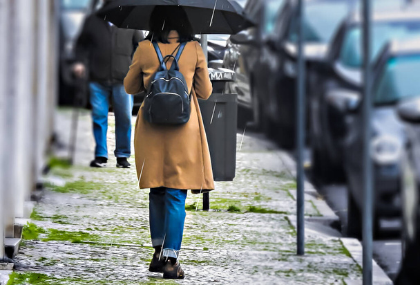 Kobieta w brązowym płaszczu spacerująca w deszczu z otwartym parasolem - Zdjęcie, obraz