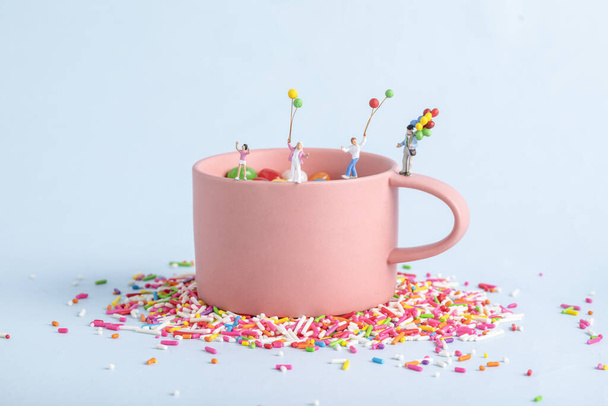 A closeup shot of human figurines with balloons playing in a pink cup with sprinkles - Foto, afbeelding