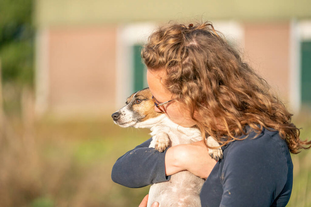 Farmer és a háziállatok iránti szeretete. Jack Russell Terrier kutyája a nők karjaiban fekszik. stabil háttér. - Fotó, kép