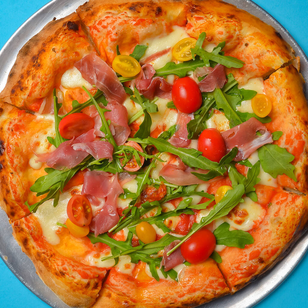 A Pepperoni pizza on a blue background isolated. Traditional Italian cuisine concept, pizza Margarita or Margherita over blue. - Foto, afbeelding