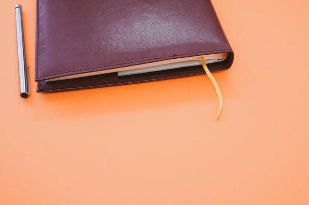 A top view closeup of a black notebook with a yellow bookmark and a pen isolated on an orange background - Photo, image