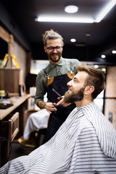 Happy young handsome man visiting hairstylist in barber shop. - Photo, Image