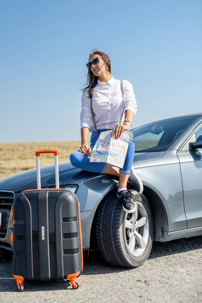 Beautiful woman   view map for travel. Pretty girl standing next to the car. The pleasure of traveling - Foto, afbeelding