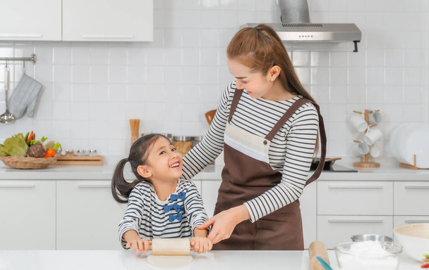 Matka uczy swoje dziecko piekarni przez walcowanie mąki na blacie kuchennym, dla koncepcji aktywności rodzinnej. - Zdjęcie, obraz