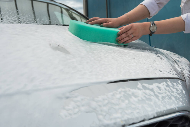 Γυναικεία χέρια με πράσινο σφουγγάρι και αφρό πλένουν το αυτοκίνητό της. Έννοια καθαρισμού. - Φωτογραφία, εικόνα
