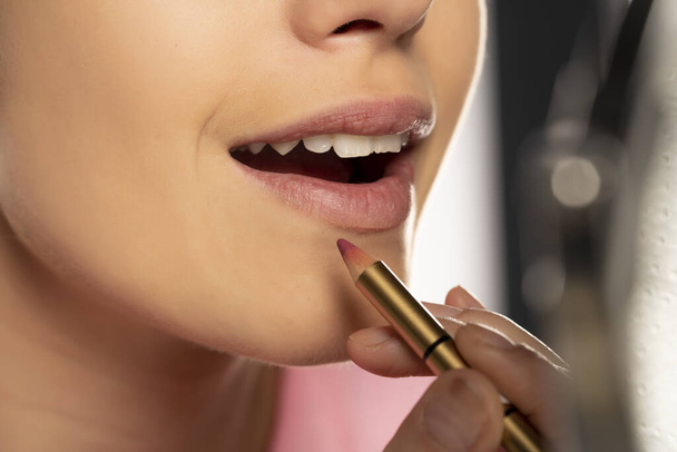 jonge vrouw toepassen lip potlood op haar lippen op witte achtergrond - Foto, afbeelding