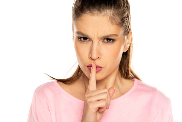 jonge boos vrouw met vinger op haar lippen op witte achtergrond - Foto, afbeelding