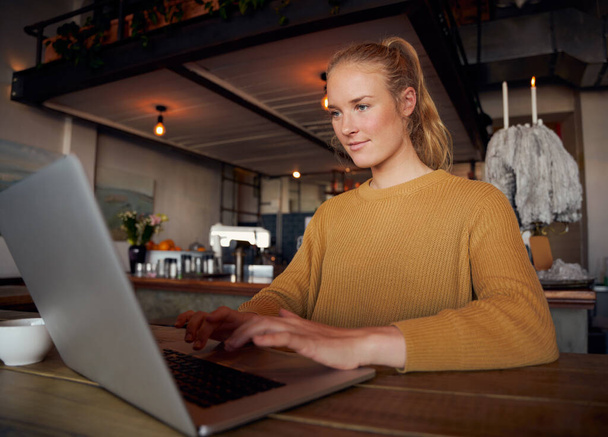Focused young female entrepreneur typing on laptop sitting in modern cafe - Fotó, kép