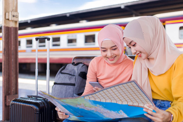 Twee moslimvrouwen keken naar de kaart en glimlachten vrolijk terwijl ze op de trein op het perron wachtten.. - Foto, afbeelding