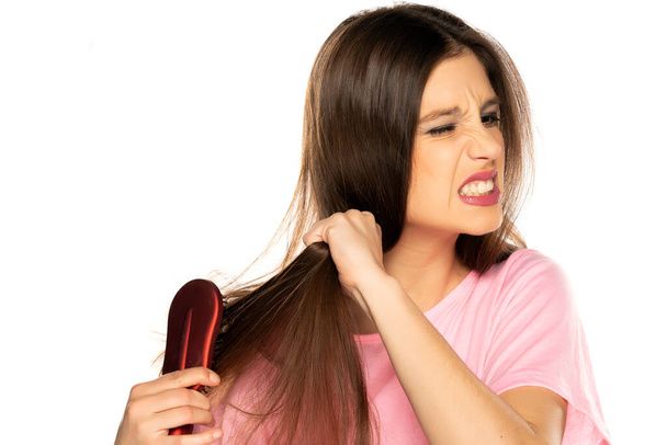 Jovem mulher nervosa escovando o cabelo no fundo branco - Foto, Imagem