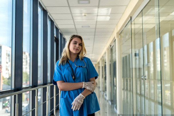 Όμορφη νοσοκόμα με μπλε στολή με στηθοσκόπιο σε εσωτερικούς χώρους στη σύγχρονη κλινική. Υπάλληλος υγειονομικής περίθαλψης στο νοσοκομείο περιμένει για τη διάγνωση των ασθενών  - Φωτογραφία, εικόνα
