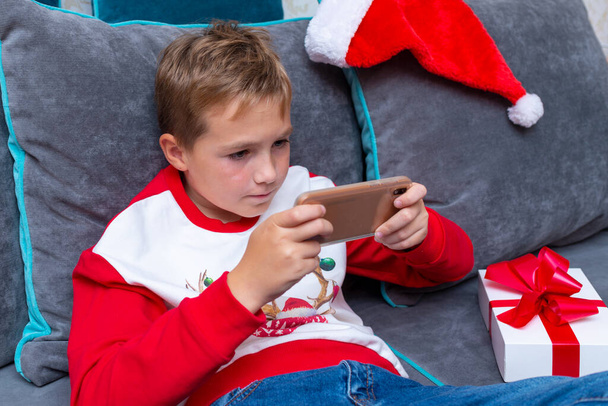 Attraktiver Junge mit Smartphone an den Weihnachtsfeiertagen weißes Geschenk zu Weihnachten Foto zu Hause.. - Foto, Bild