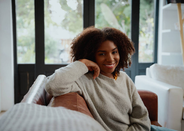 Cheerful black woman with curly hair relaxing on sofa looking at camera - Foto, afbeelding