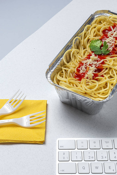 Lunch at workplace homemade and healthy spaghetti with tomato and cheese on work table with computer keyboard. Home food for office concept. Take away food - Photo, Image