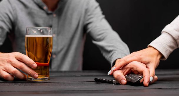 Cropped image of man olding glass of beer with car key on wooden table in splash colors technique, create idea of drinking and driving is definitely arrest concept - Photo, Image