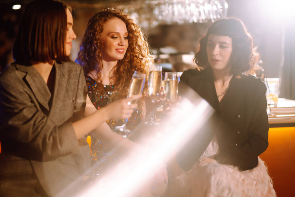 Τρεις γυναίκες με ποτήρια σαμπάνιας σε ένα πάρτι. Οι φίλες κάνουν πρόποση για τις χειμωνιάτικες διακοπές μαζί στο μπαρ. Φίλοι, μπάτσελορ πάρτι, γενέθλια, έννοια χειμερινές διακοπές. - Φωτογραφία, εικόνα