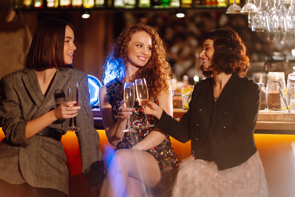 Three Woman with glasses of champagne  at a party. Women friends make a toast elebrating winter holidays together in bar. Friends, bachelorette party, birthday, winter holidays concept. - Valokuva, kuva