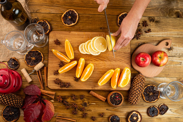 Woman hands slicing orange, cutting citrus fruits. Knife, wooden cutting board, juice squeezer, closeup. Making homemade lemonade - 写真・画像