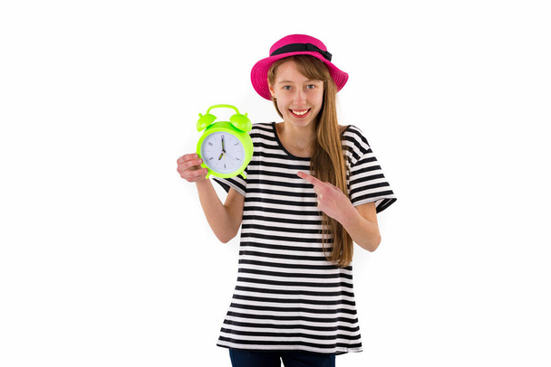 Teen Girl stochern beim Wecker, isoliert auf weißem Hintergrund. Porträt eines kaukasischen Teenagers mit grünem Wecker. - Foto, Bild