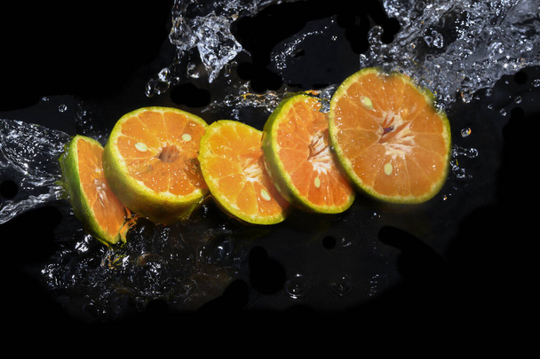 Orangen in Scheiben geschnitten auf der Wasseroberfläche vor schwarzem Hintergrund - Foto, Bild
