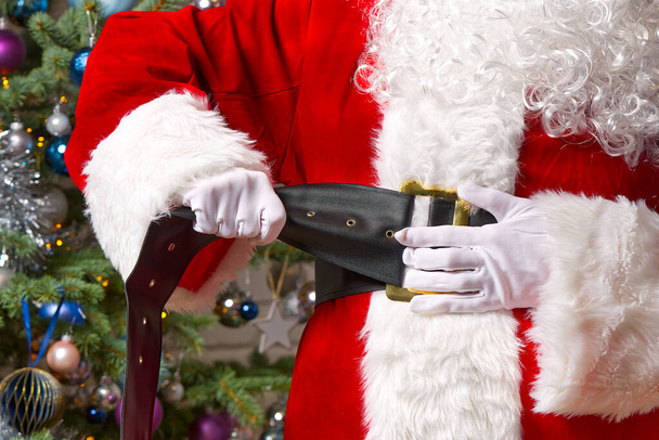 Санта Клаус притискає ремінь до свого великого живота. - Фото, зображення