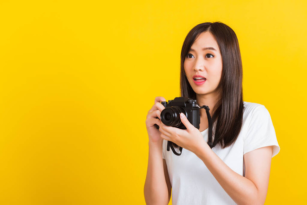 Portrait of happy Asian beautiful young woman photographer holding vintage digital mirrorless photo camera on hands, studio shot isolated on yellow background, lifestyle teenager hobby travel concept - Photo, Image
