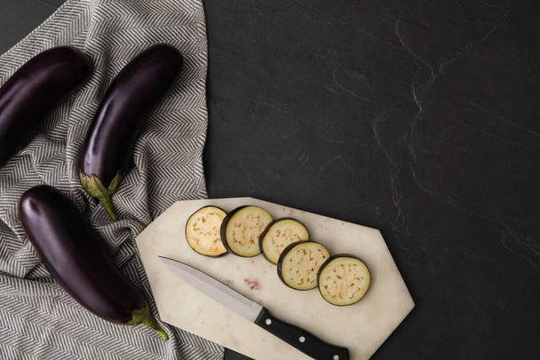 Cut and whole raw ripe eggplants on black table, flat lay. Space for text - Фото, зображення