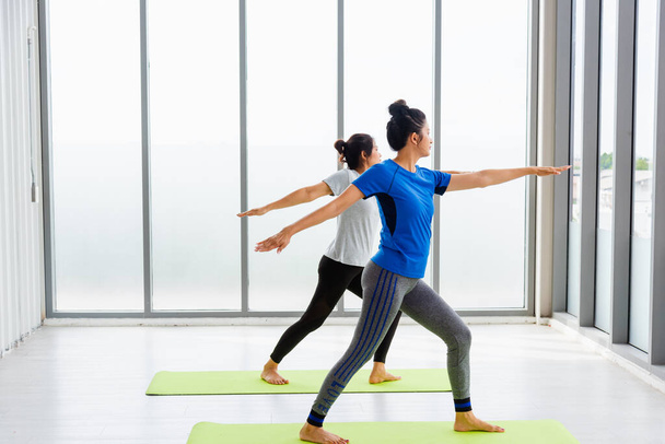 Two Asian women sporty attractive people practicing yoga lesson together, working out at the fitness GYM, Young and senior female exercising do yoga in yoga classes, sport healthy lifestyle - Foto, afbeelding