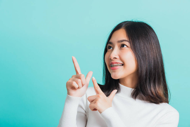 Portrait of Asian teen beautiful young woman smile have dental braces on teeth laughing point finger side away blank copy space, studio shot isolated on blue background, medicine and dentistry concept - Fotoğraf, Görsel