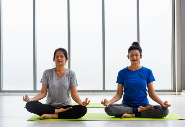 Two Asian women sporty attractive people practicing yoga lesson together, working out at the fitness GYM, Young and senior female exercising do yoga in yoga classes, sport healthy lifestyle - Photo, Image