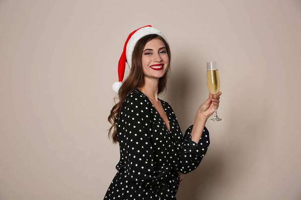 Happy woman in Santa hat with champagne on beige background. Christmas party - Photo, image