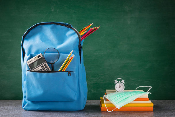 Front school backpack and accessories with face mask protect on table at chalkboard, student bag supplies at classroom backboard, Back to school education new normal outbreak COVID-19 or coronavirus - 写真・画像