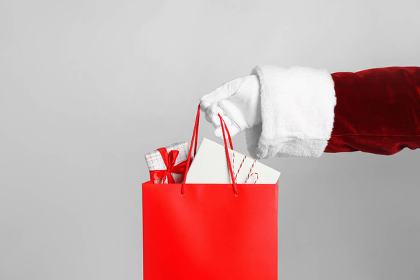 Santa holding paper bag with gift boxes on light grey background, closeup - Fotó, kép