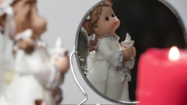 クリスマスや新年のためのライト付きの赤いキャンドルを持つクリスマスや新年の天使。鏡の中には天使の姿が灰色の背景に映し出されている。12月の休日と宗教と占い - 映像、動画