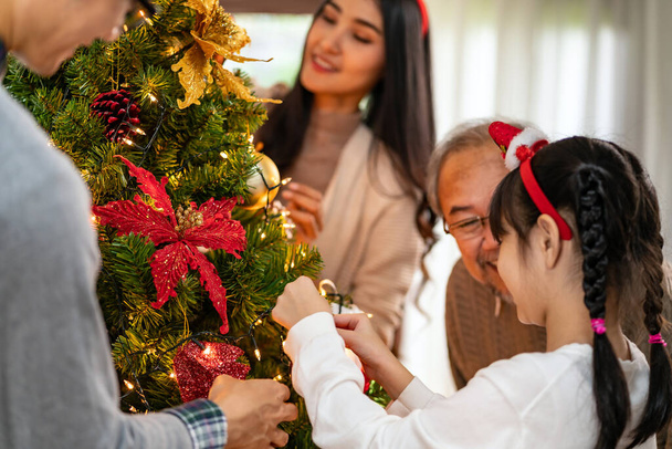 Multigenerational asian Family decorating a Christmas tree. Mom Dad daughter girl and grandfather decorate the Christmas tree prepare for season greeting of Merry Christmas and Happy Holidays. - Φωτογραφία, εικόνα