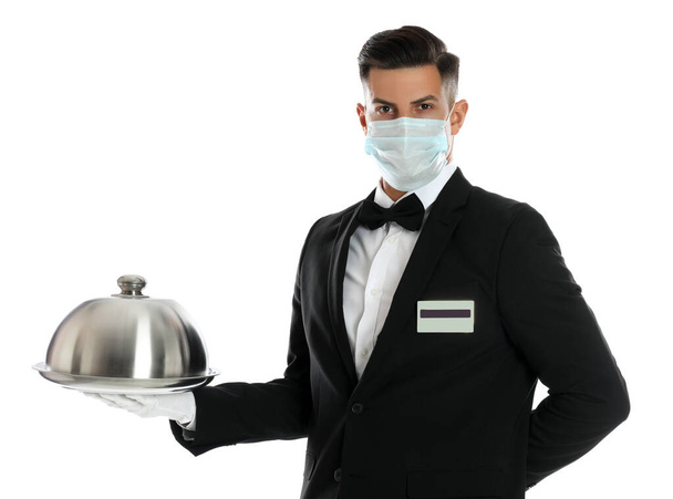 Waiter in medical face mask holding tray with lid on white background - Valokuva, kuva