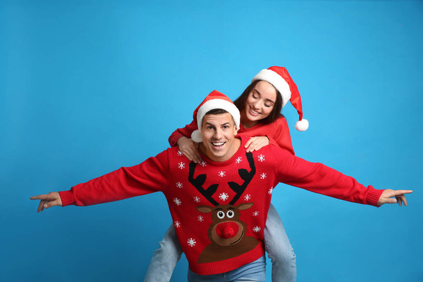 Couple in Christmas sweaters and Santa hats on blue background - Foto, Imagem