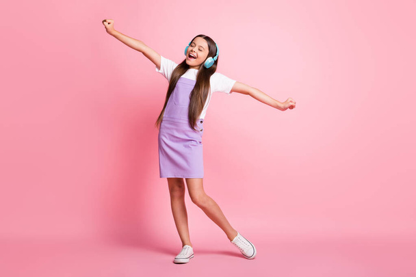 Full size photo of excited kid girl listen wireless headset music sing wear violet overall isolated on pastel color background - 写真・画像