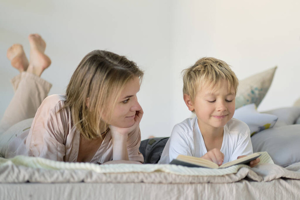 Mamá enseña a su hijo que leer un libro está en la cama en casa. Conceptos educativos. Colores pastel, enfoque selectivo. - Foto, imagen
