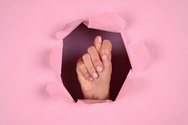 Vrouwelijke hand tonen vijg of duim gebaar op roze achtergrond. - Foto, afbeelding