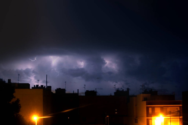 temporale notturno con fulmini tra nuvole ed edifici cittadini in primo piano - Foto, immagini