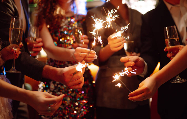 Sparkling sparklers in the hand. Group of happy people holding sparklers at the party. Young friends clinking glasses of champagne  in a nightclub. Celebration, people and holidays concept. - Foto, Imagem