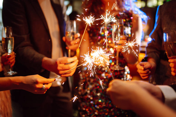 Sparkling sparklers in the hand. Group of happy people holding sparklers at the party. Young friends clinking glasses of champagne  in a nightclub. Celebration, people and holidays concept. - Fotoğraf, Görsel
