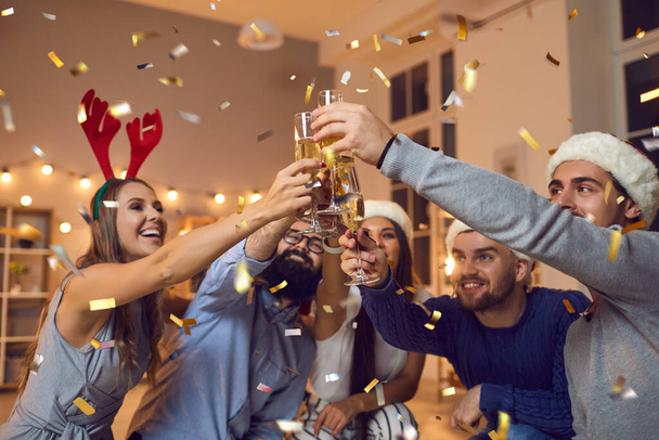 Group of young positive friends in decorative hats celebrating Christmas with champagne during party - Фото, зображення