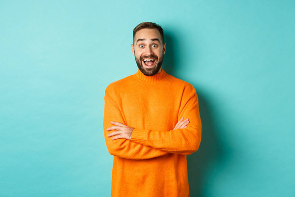 Kuva onnellinen ja yllättynyt mies reagoi uutisia, näyttää hämmästynyt, seisoo oranssi pusero vastaan turkoosi tausta - Valokuva, kuva