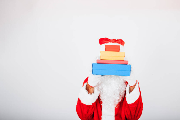 Kerstman op witte achtergrond deelt gekleurde cadeau pakketten die zijn gezicht bedekken. - Foto, afbeelding