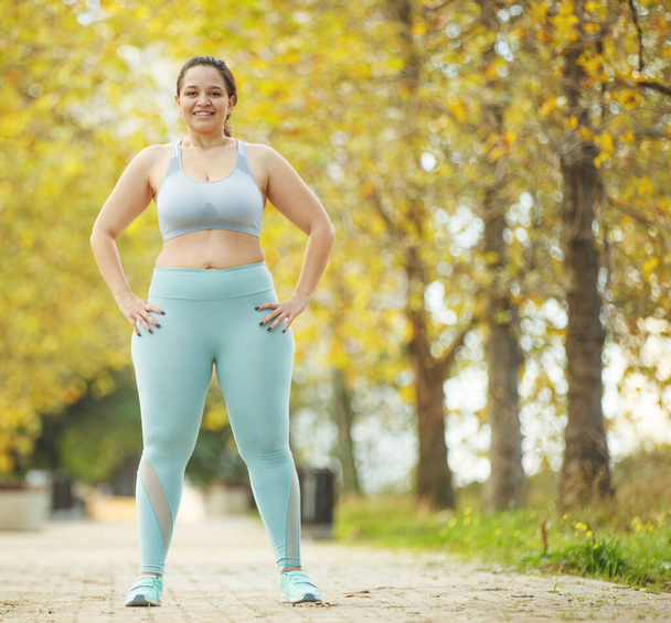 An attractive plus size woman in a sports top and leggings, goes in for sports, works out in a cozy city park. - Photo, Image