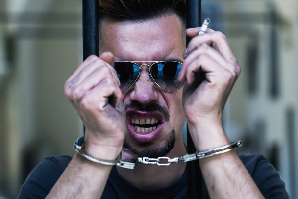 Засуджений в наручниках чоловік з цигаркою, ув'язнений за злочини, покараний за серйозну лиходію. Арешт, бандит, концепція болю
. - Фото, зображення