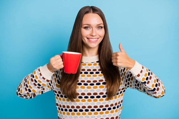 Photo of young woman dressed ornament pullover drinking tea red cup showing thumb up isolated blue color background - Fotó, kép